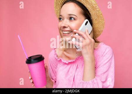 Happy young woman talking on mobile phone while having coffee on pink background Stock Photo