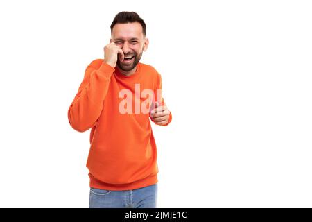 A man in an orange sweater laughs holding his hands to his stomach and face on a white background Stock Photo