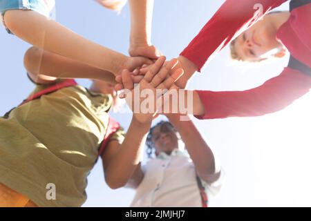 Directly below shot of multiracial elementary schoolboys stacking hands against sky during sunny day Stock Photo