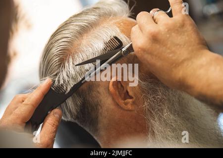 Hairdresser making stylish haircut for old man Stock Photo