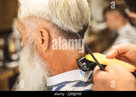 Hairdresser making stylish haircut for old man Stock Photo