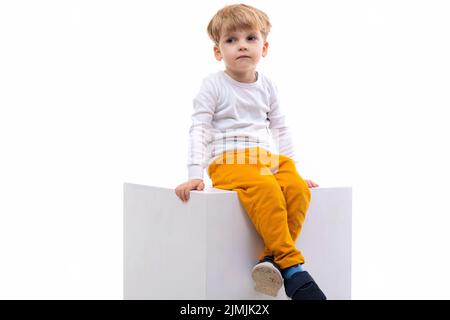 Sad bored blond boy sitting on white background Stock Photo