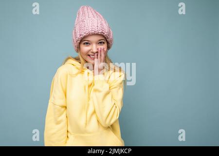 Attractive smiling happy young blond woman standing isolated over colorful background wall wearing everyday stylish outfit showi Stock Photo