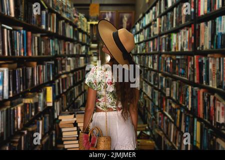 Beautiful girl wearing stylish outfit looking for interesting book in the vintage bookstore Stock Photo