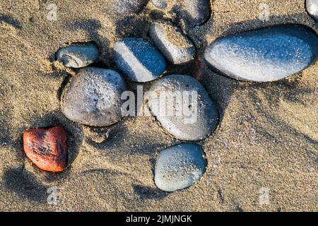 Sea pebbles on sandy beach in afternoon light. Suitable as background or zen style decoration. Stock Photo