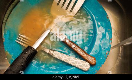 A dirty fork and spoon on a blue plate in a dishwasher Stock Photo