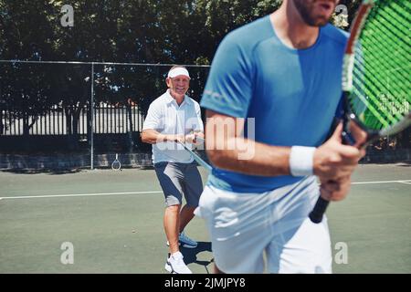 Youre doing great. two handsome sportsmen using resistant bands during a tennis training session during the day. Stock Photo