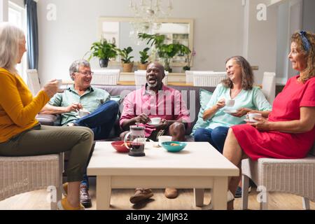 Happy multiracial senior female and male friends talking while having coffee together at home Stock Photo