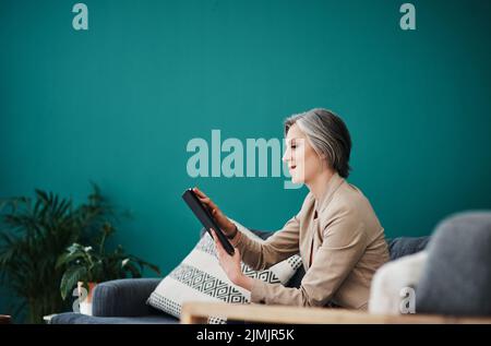 Checking my emails on any device. an attractive mature businesswoman sitting alone and using a tablet in her home office. Stock Photo