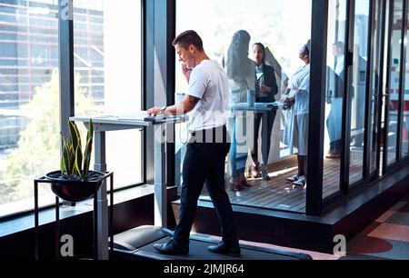 Walk and work your way to success. a young businessman talking on a cellphone and going through paperwork while walking on a treadmill in an office. Stock Photo