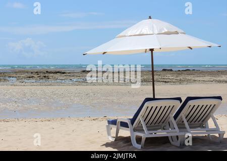 Beach landscape with two sunbeds and parasol on the sand, with sea and sky. Stock Photo