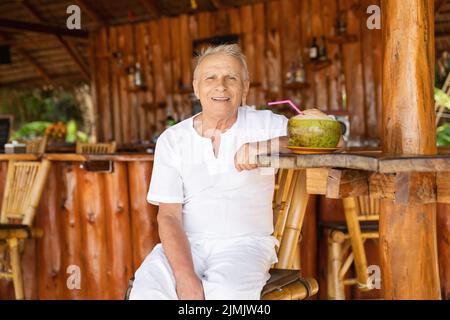 Happy senior man is drinking a coconut water in the beach bar Stock Photo