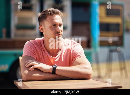 What a view. a cheerful man seated at a table by himself outside next to a beach promenade during the day. Stock Photo