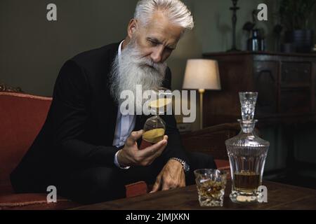 Handsome and bearded senior man drinking whiskey Stock Photo