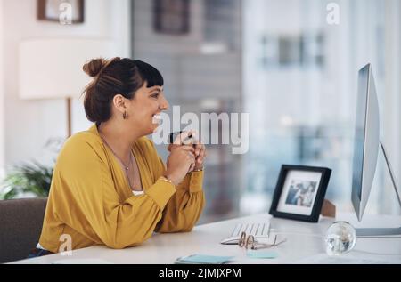 Coffee gets me through my busy day. an attractive young businesswoman sitting in her office and holding a coffee cup while using her computer. Stock Photo