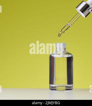 Essential oil falling from the amber glass dropper. White bottle of cosmetic oil with a pipette, green background Stock Photo