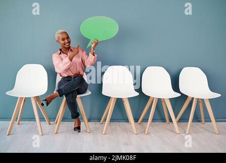 Check this out guys. Studio portrait of an attractive young businesswoman pointing to a speech bubble while siting in line against a grey background. Stock Photo