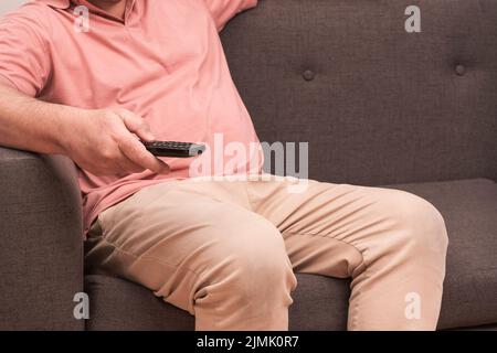 unrecognizable man sitting on a sofa with a remote control in his hand changing channels on the television. concept of rest and relaxation Stock Photo
