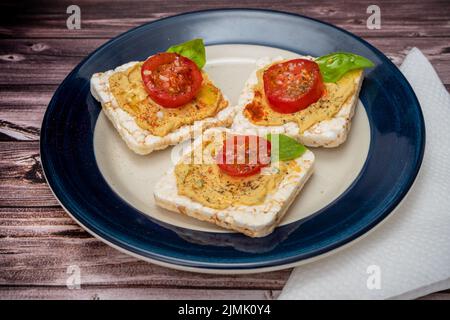 Three Rice crackers with chickpea hummus, cherry tomato and fresh basil on a plate on a rustic table. Healthy food. Stock Photo