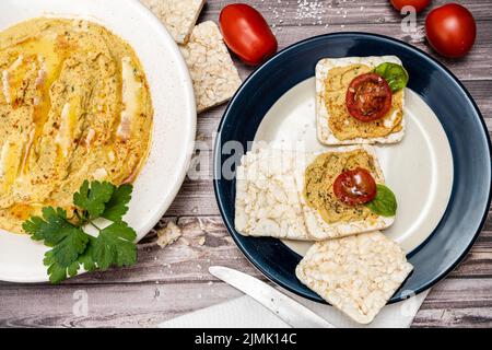 Square rice crackers with hummus and cherry tomatoes on a plate. Tomatoes, crackers on a rustic table and a platter with hummus. Natural and healthy f Stock Photo