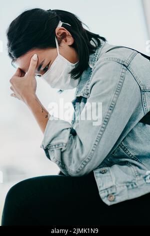 These are stressful times we live in. a young woman experiencing a headache and wearing a mask while waiting in a doctors office. Stock Photo