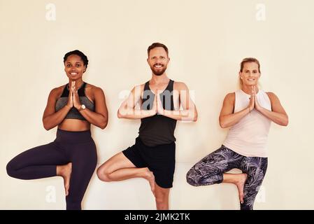 Experience the now with yoga. a group of young men and women practicing the tree pose during a yoga session. Stock Photo