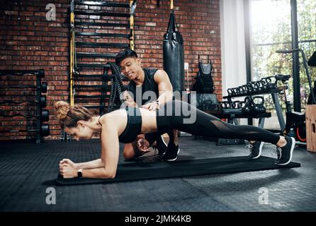 Youll never regret getting a personal trainer. a young woman working out with her personal trainer. Stock Photo