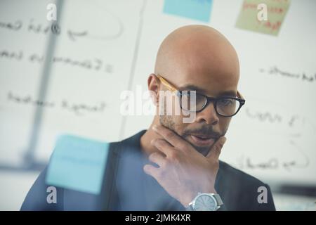 Its taking me longer than expected to solve this. a young businessman brainstorming with notes on a glass wall in an office. Stock Photo