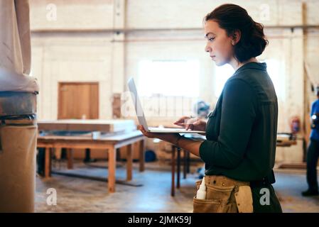 I want to try some of these designs. a female carpenter using a laptop in her workshop. Stock Photo