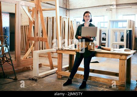 Your home could do with one of our pieces. a female carpenter using a laptop in her workshop. Stock Photo