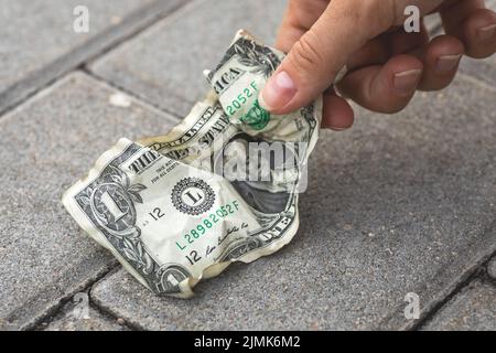 Poor woman picking old and crumpled one dollar bill Stock Photo