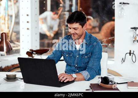 Everything is working in my favor today. a handsome young businessman working on a laptop in an office inside his workshop. Stock Photo