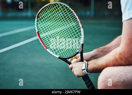 Today I will advance to a new level. Closeup shot of an unrecognisable man holding a tennis racket and ball on a tennis court. Stock Photo