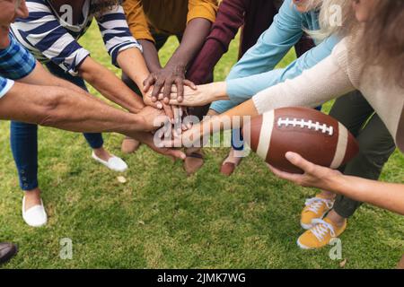 Multiracial senior male and female friends stacking hands while playing rugby in backyard on weekend Stock Photo