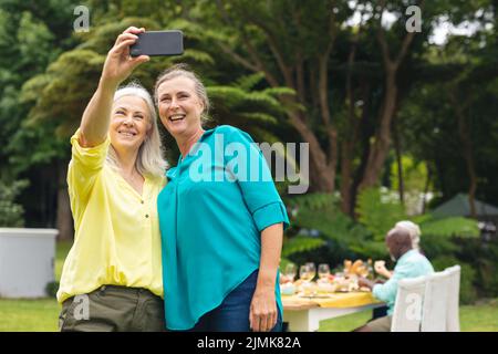 Happy caucasian senior women taking selfie through smart phone during backyard party Stock Photo
