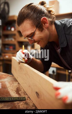 Making my mark. a focused young carpenter doing measurements on a piece of wood inside of a workshop at night. Stock Photo