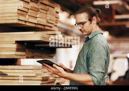 Make technology work in your favor. a young carpenter using a digital tablet while working inside his workshop. Stock Photo