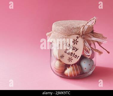 Happy Easter. Colourful painted easter eggs in glass jar on pink background, Christian religion and holiday Stock Photo