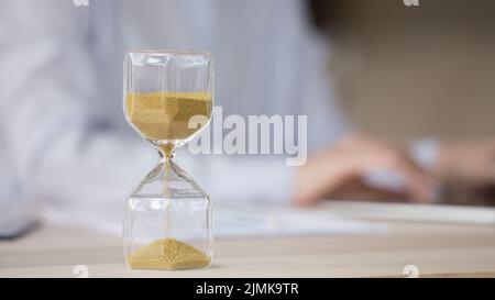 Sand watch object close up with hands typing on laptop Stock Photo