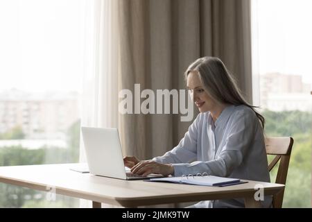 Focused positive elderly lady using laptop computer indoors Stock Photo