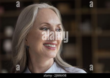 Happy senior lady looking away with thoughtful satisfied toothy smile Stock Photo