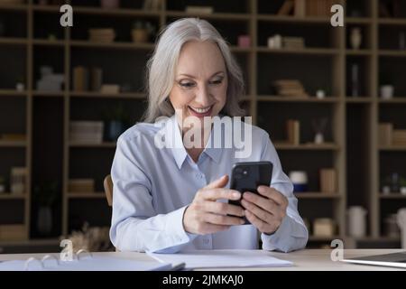 Cheerful elderly business woman using smartphone at home Stock Photo