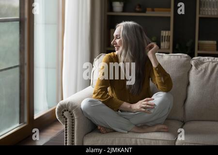 Happy pretty mature grey haired woman resting on cozy sofa Stock Photo