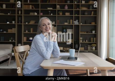 Happy cheerful elderly entrepreneur woman posing at home work table Stock Photo