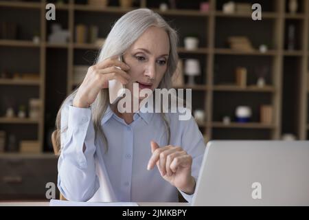 Serious elderly freelance business woman engaged in phone conversation Stock Photo