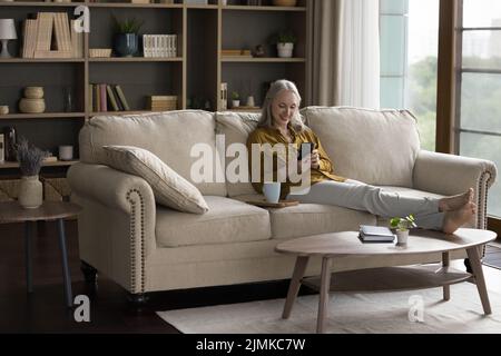 Happy joyful mature woman using mobile phone at home Stock Photo