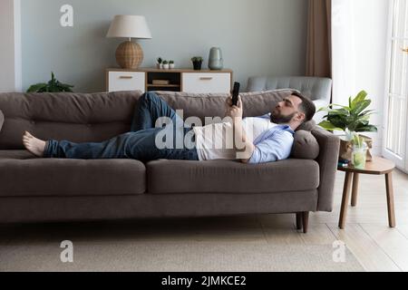 Man use modern smartphone lying on sofa in living room Stock Photo