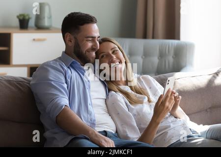 Pretty laughing couple relaxing on sofa using smartphone Stock Photo