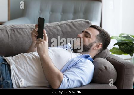 Single man lying on sofa with smartphone Stock Photo