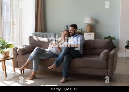 Couple relaxing on sofa spend time on internet using smartphone Stock Photo